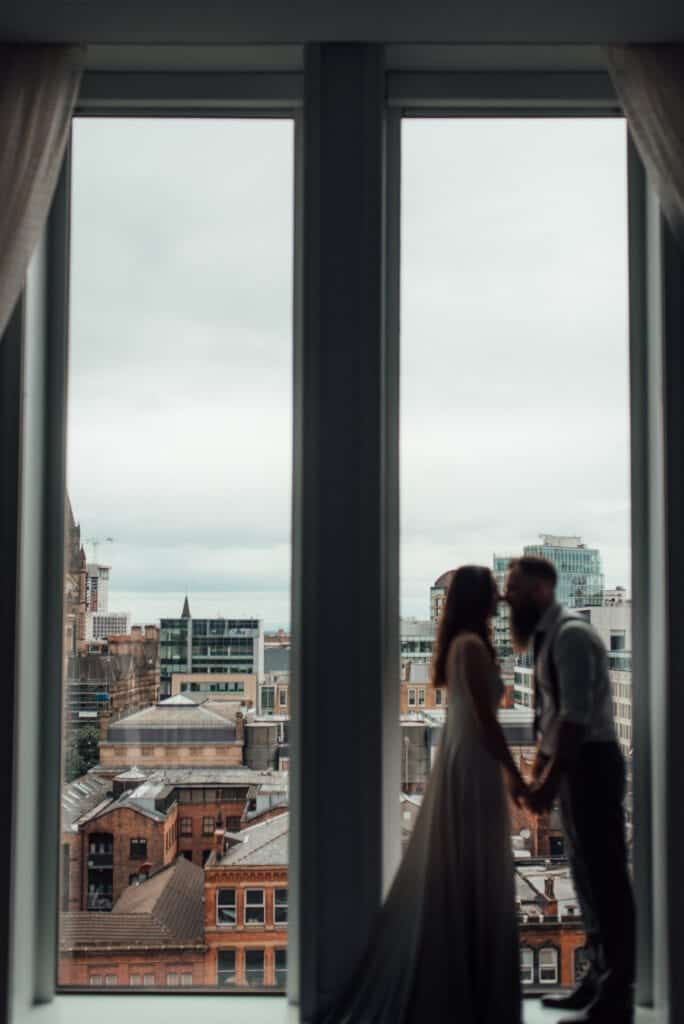 couple stood in front of city hotel window with skyline behind 