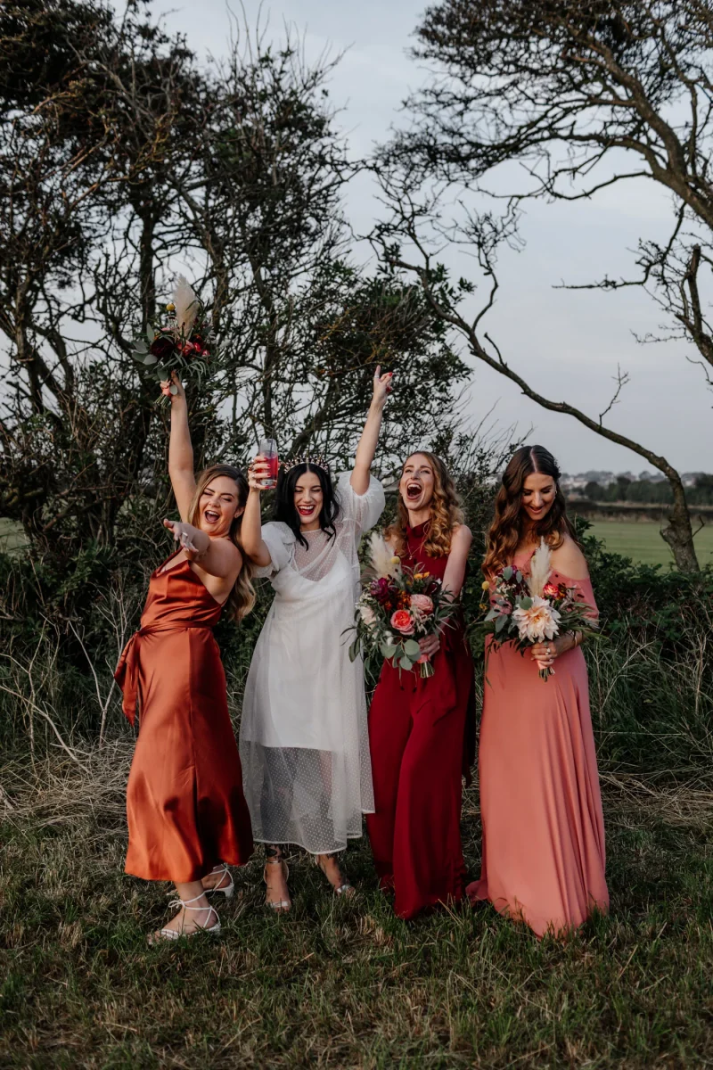 bridesmaids in mismatched orange, coral and red bridesmaid dresses