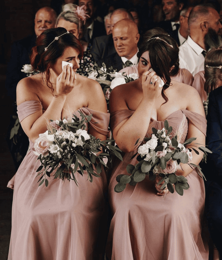 two bridesmaids crying at a wedding wearing satin pink dresses