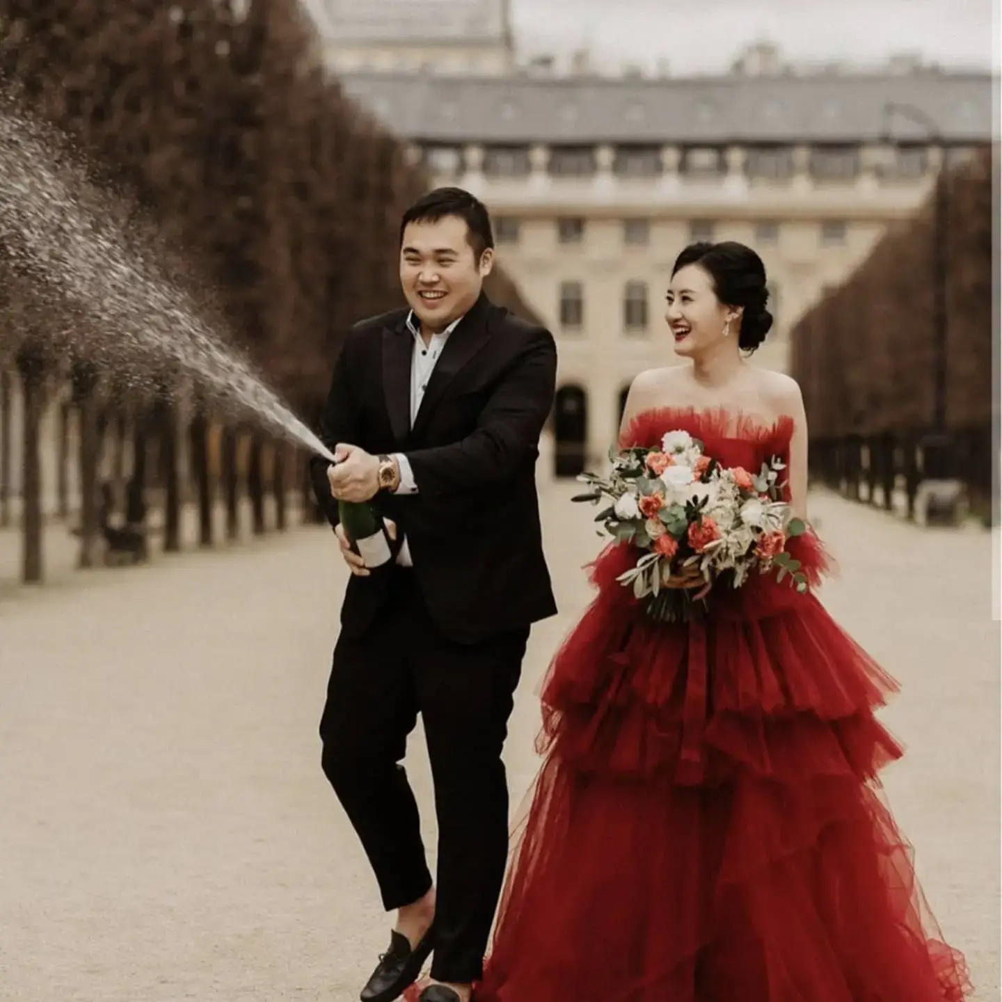 bride in tulle red dress with white pink and red bouquet and groom in black suit