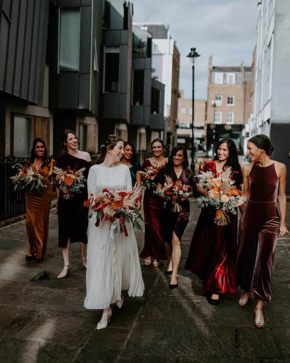 bride and bridesmaids walking down city street in red velvet bridesmaid dresses