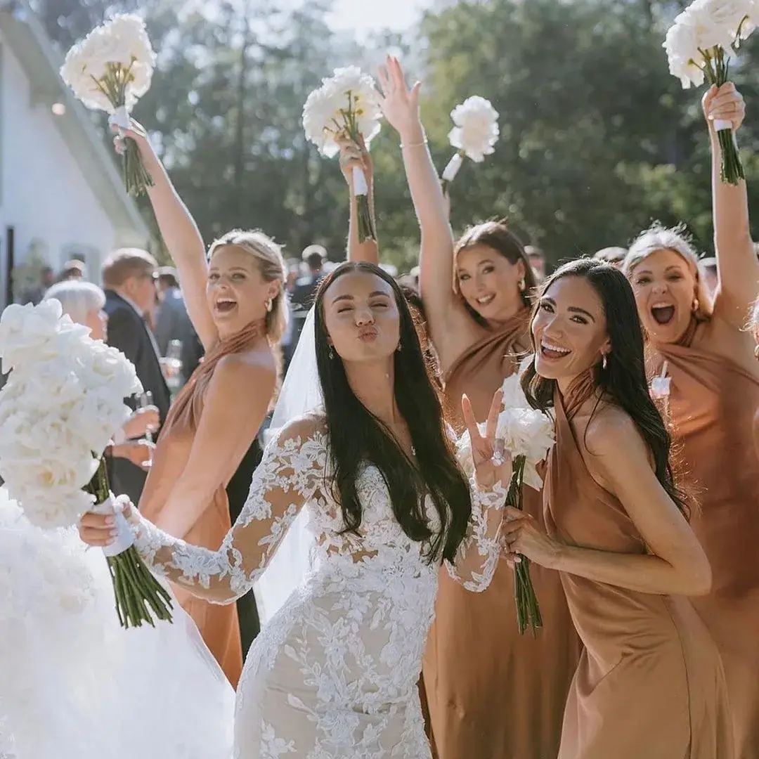bride in lace dress with bridesmaids in light copper dresses with white bouquets