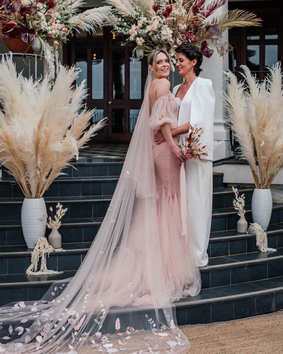bride and bride on steps, bride in pink dress also has long pink veil with floral embroidery, no jewellery simple white and pink bouquet  