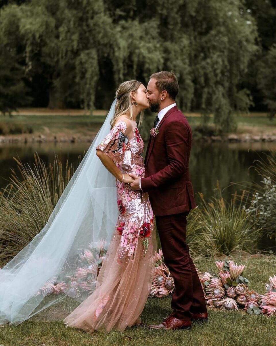 bride in pink sequin wedding gown with red florals, groom in matching red suit 
