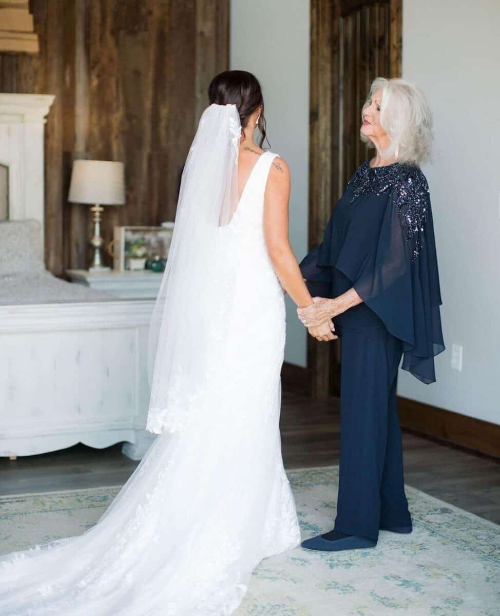 mother of the bride in blue trouser suit holding brides hand