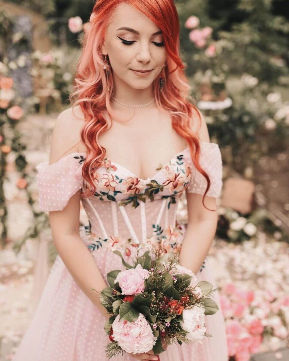 bride in embroidered pink floral wedding dress, pink hair down, pink and green bouquet and pearl earrings 
