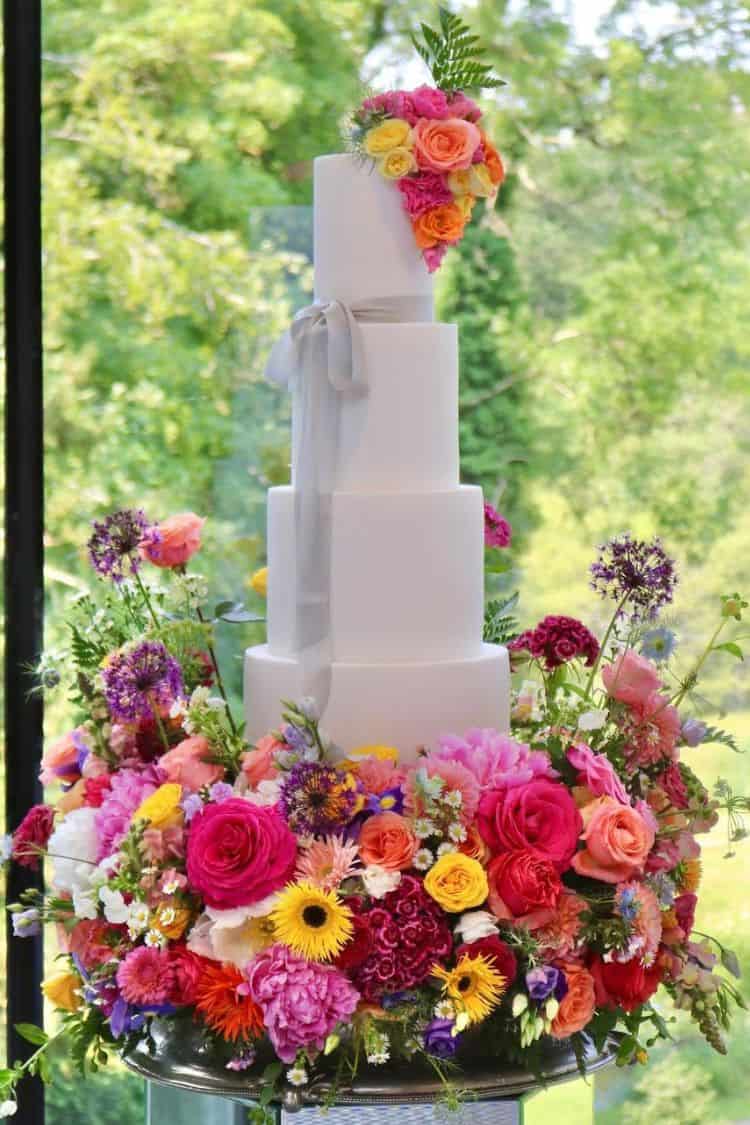 simple white wedding cake surrounded by bright and bold summer flowers