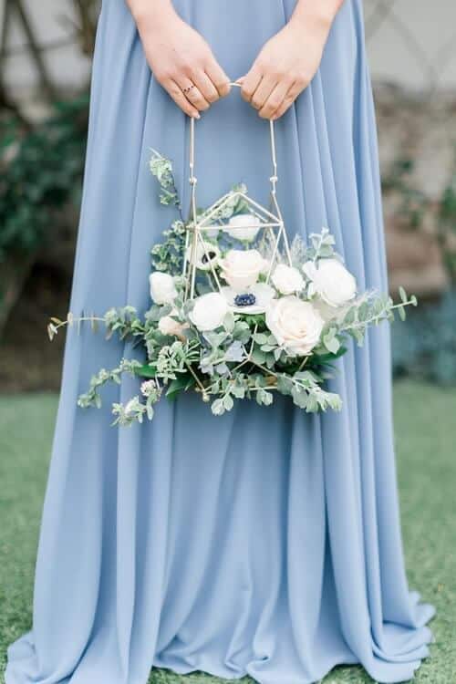 bridesmaid holding a gold geometric lantern with white flowers and greenery