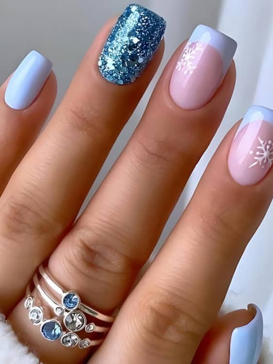 This nail design combines soft pastel blue with a mix of glitter and delicate snowflake details. 