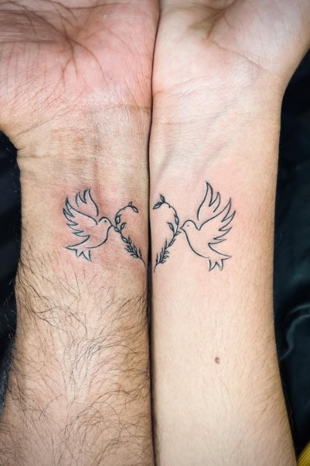 arms joining to show a heart with two birds tattoo