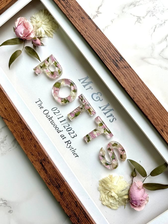 a wooden frame with resin letters made from wedding flowers saying 'potts' 